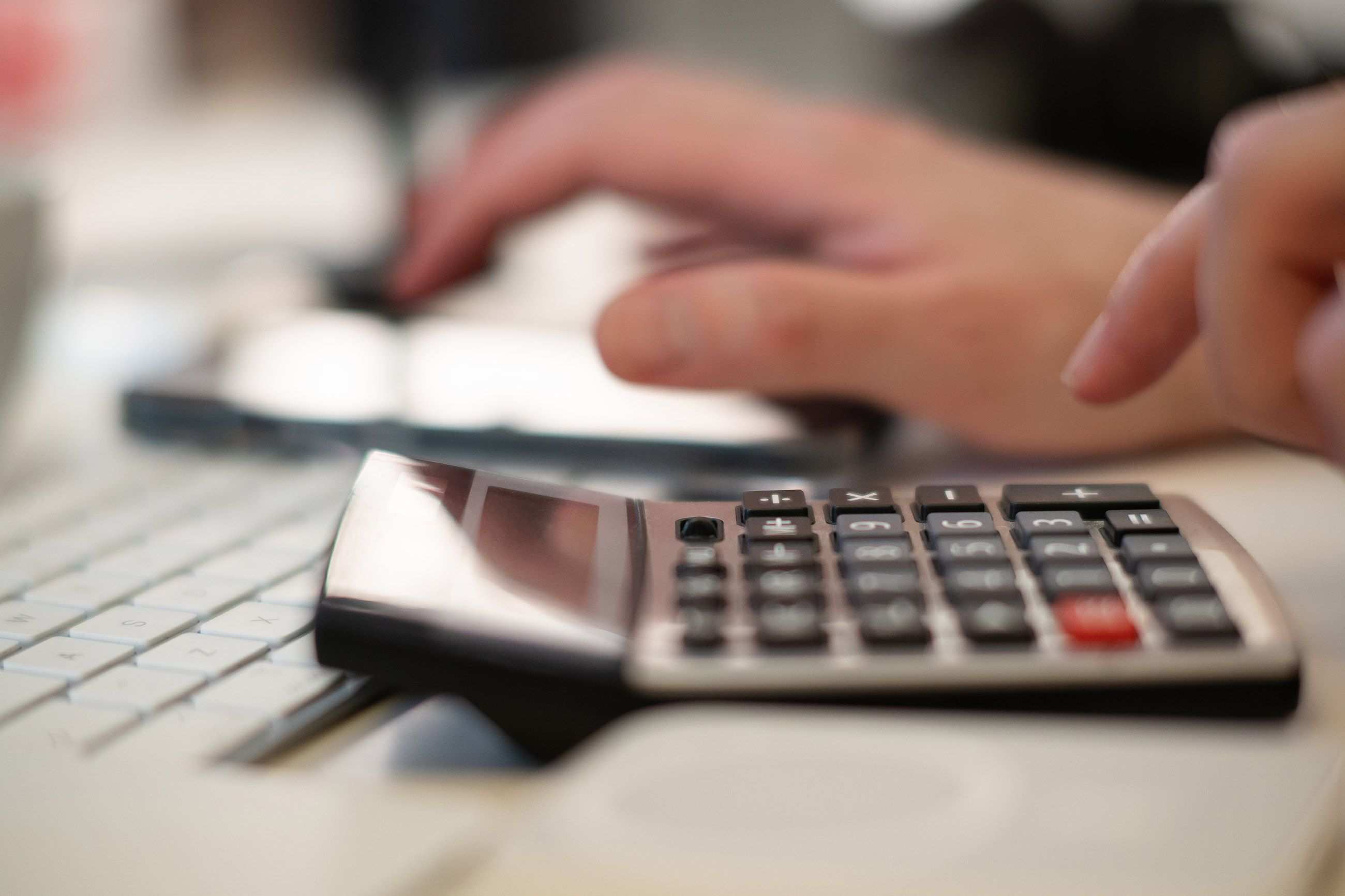 Hände an einer Tastatur neben einem Taschenrechner und einem offenen Kassenbuch in einer finanziellen Arbeitsumgebung